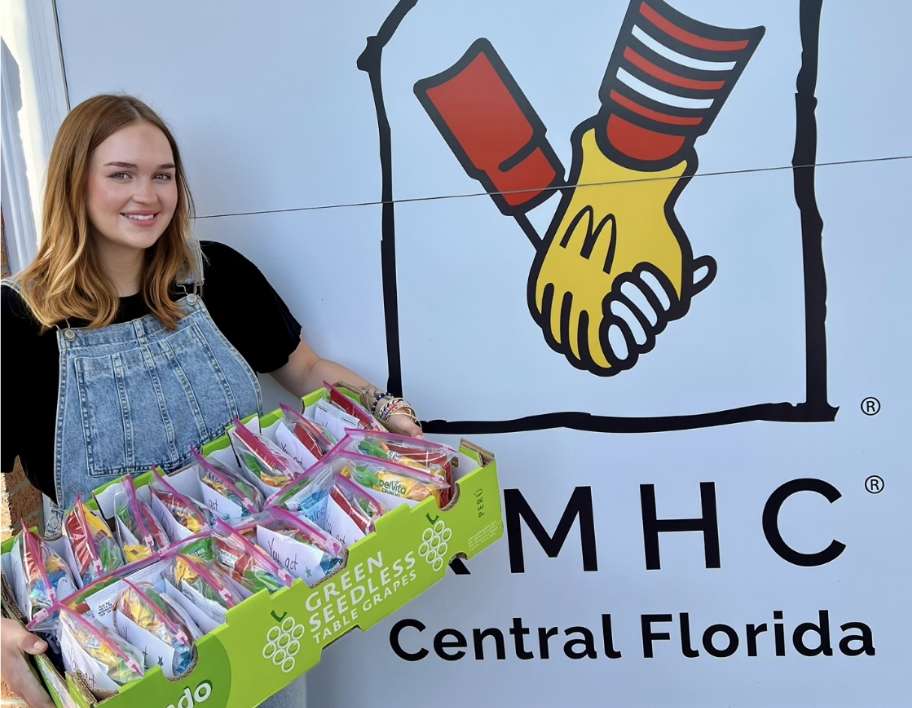 A woman holding packages of food in front of an RMHC Central Florida logo