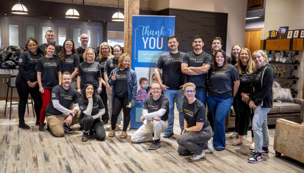 A group of people in front of a "Thank You" sign wearing shirts that read "We Care at Healthpeak"